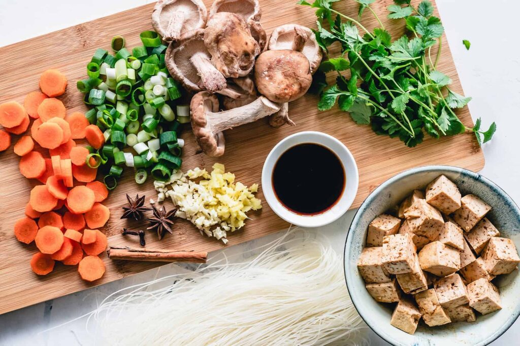 pexels-ella-olsson-3026802 - RIM Digital Chopped carrots, green onions, mushrooms, and cilantro with tofu cubes and soy sauce on a wooden cutting board—prepping a dish.