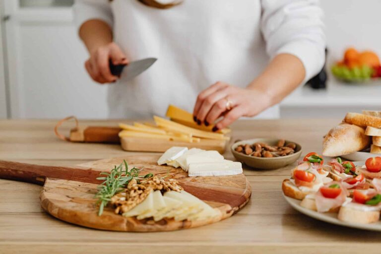 pexels-karolina-grabowska-6660203 - RIM Digital Person slicing cheese and arranging a rustic charcuterie board with bread, nuts, and herbs on a wooden table in a bright kitchen