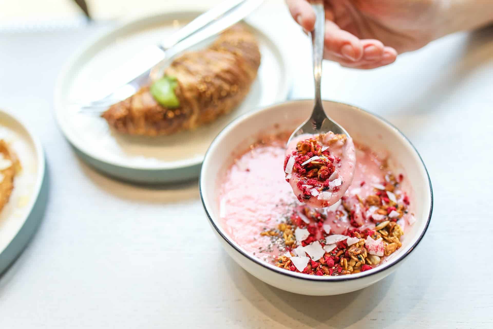 pexels-polina-tankilevitch-3872263 - RIM Digital Pink yogurt with granola and coconut flakes in a bowl, spoonful being lifted for a bite.