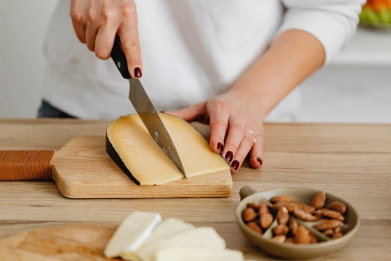 pexels-polina-tankilevitch-45190532 - RIM Digital Hands slice cheese on a wooden cutting board with a knife, nuts in a bowl nearby