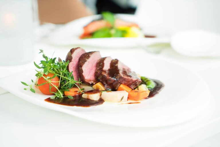 pexels-terje-sollie-299347 - RIM Digital Sliced medium-rare beef with dark glaze on a bed of diced carrots and potatoes, garnished with fresh greens on a white plate.