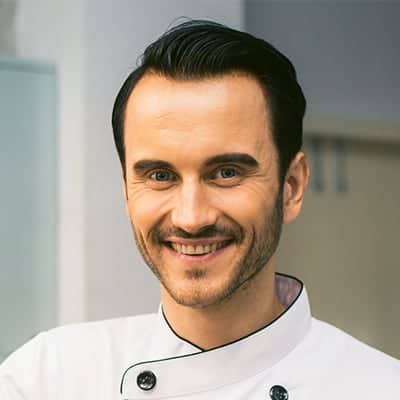 pexels-tirachard-kumtanom-887827 - RIM Digital Smiling male chef in a white chef coat, standing in a kitchen.