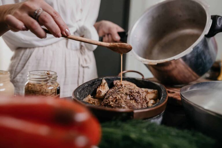 vitor-monthay---mnzh75wZ4-unsplash - RIM Digital Hands spooning brown sauce over roasted meat in a skillet, jar of ingredients nearby