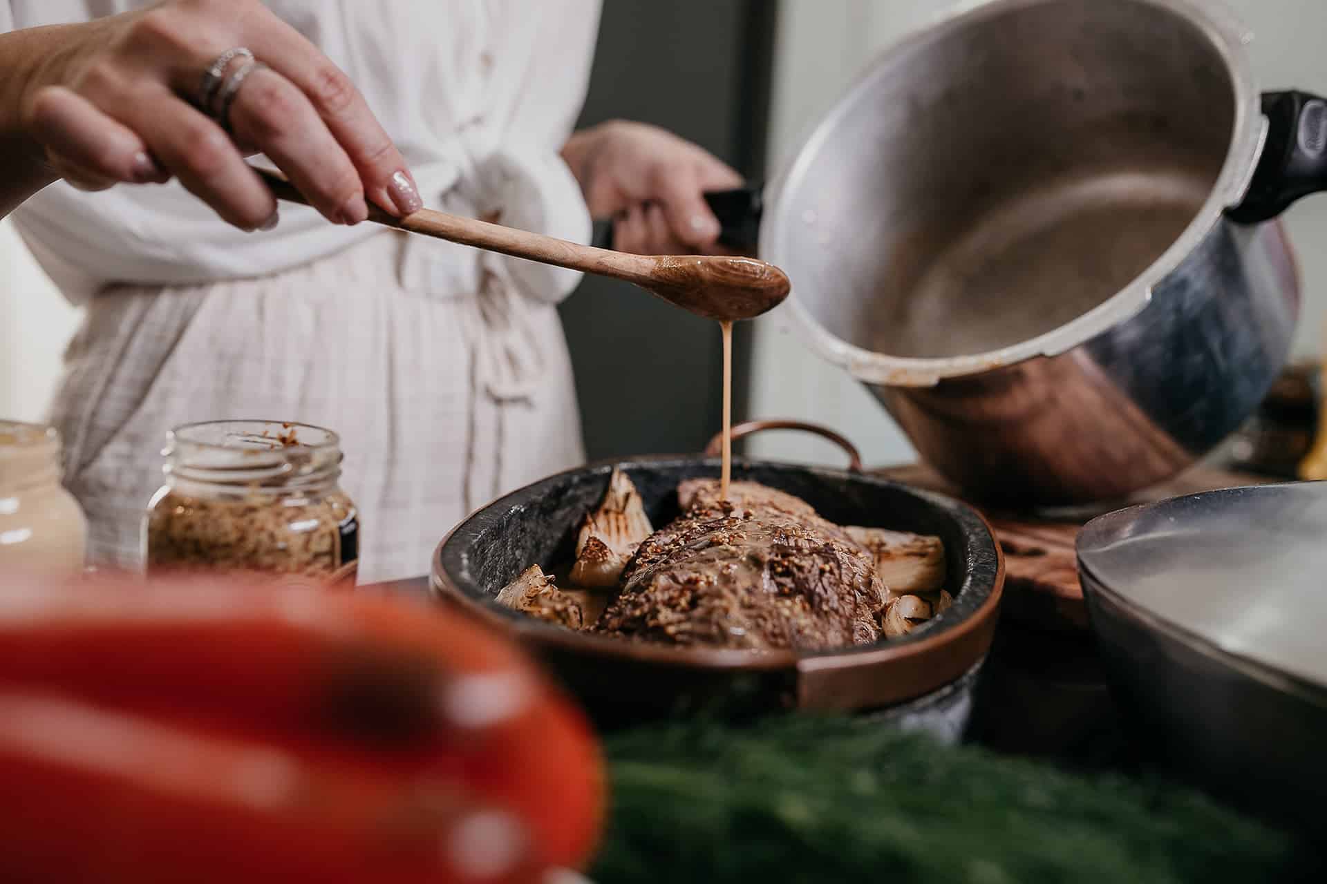 vitor-monthay---mnzh75wZ4-unsplash - RIM Digital Hands spooning brown sauce over roasted meat in a skillet, jar of ingredients nearby