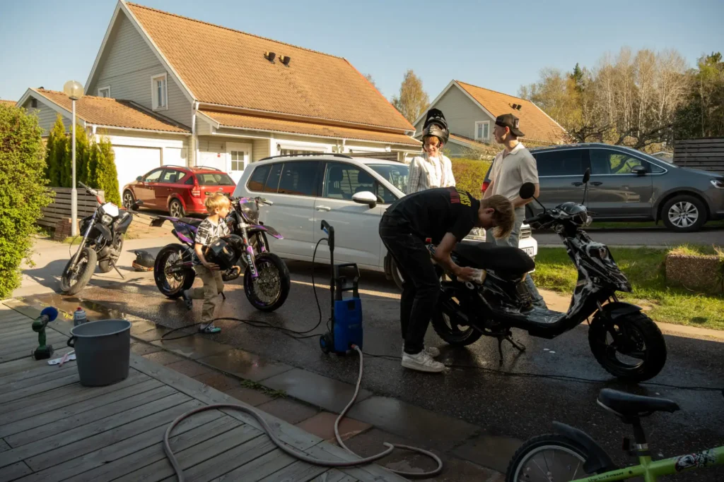 Tre mopeder och tre ungdomar tvättar moped på en garageuppfart i Enköping.