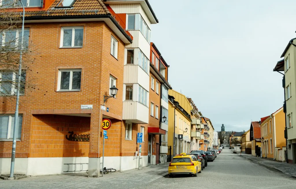 Kyrkogatan i Enköping 2023 med moderniserad stadsmiljö – asfalt, buskar, bilar och nya fasader kontrasterande mot den historiska bilder.