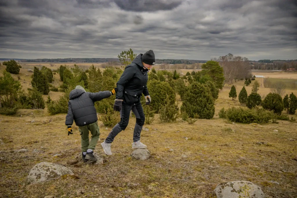 Två personer som vandrar på en kuperad stig genom Vånsjöbroåsen med molnig himmel ovanför.