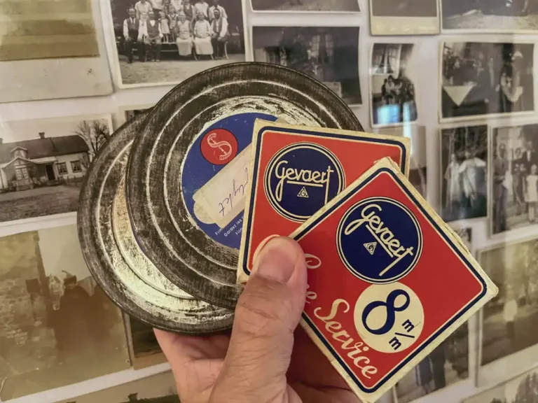 Hand håller gamla 8 mm-filmrullar från 1940-talet framför ett kollage av svartvita familjefoton.